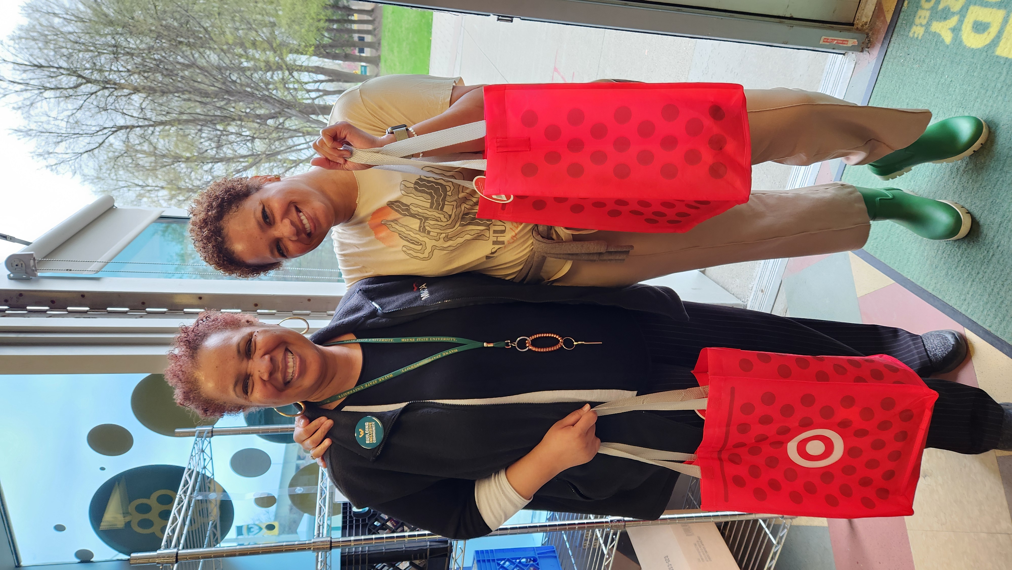 two people standing and smiling while holding tote bags
